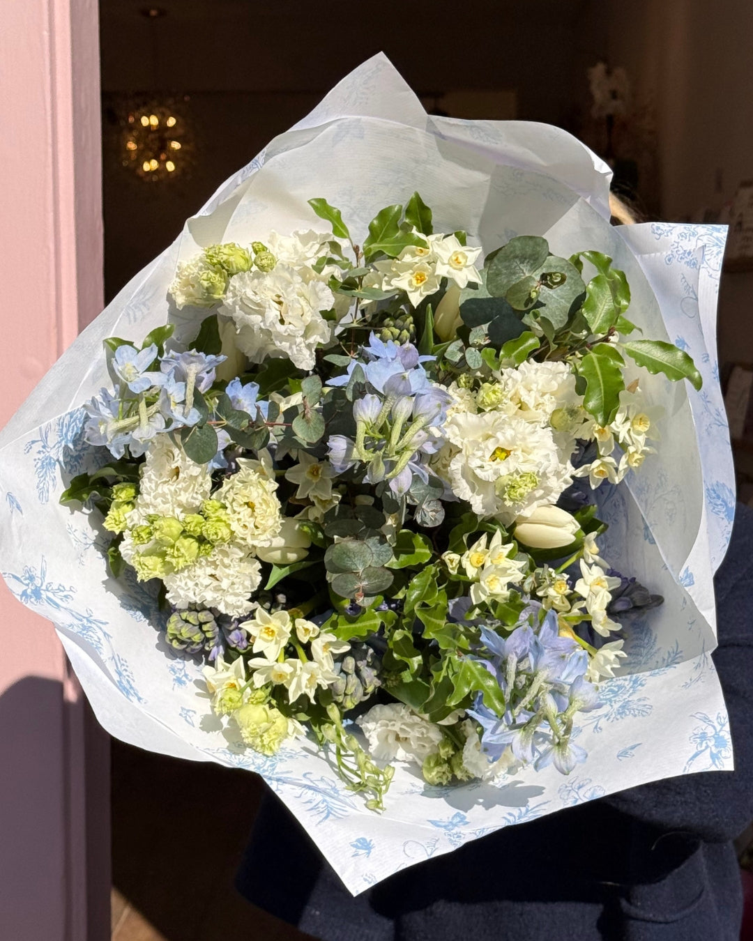 Bouquet of flowers wrapped in white paper with blue floral patterns, held by a person.