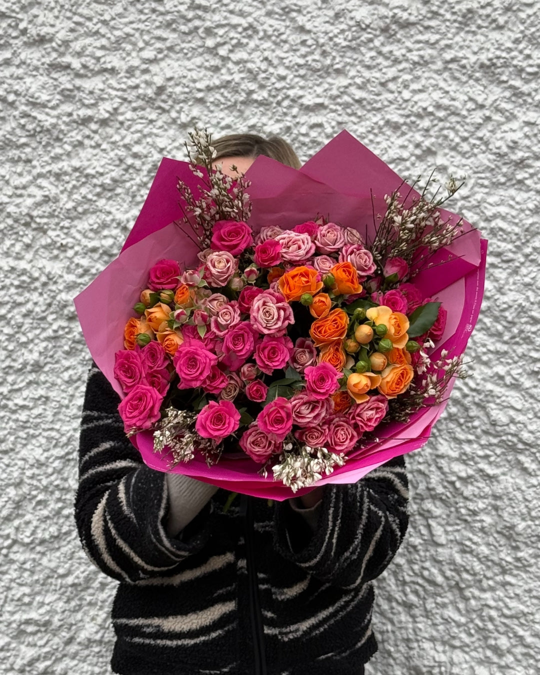Person holding a colorful bouquet of flowers against a textured wall.