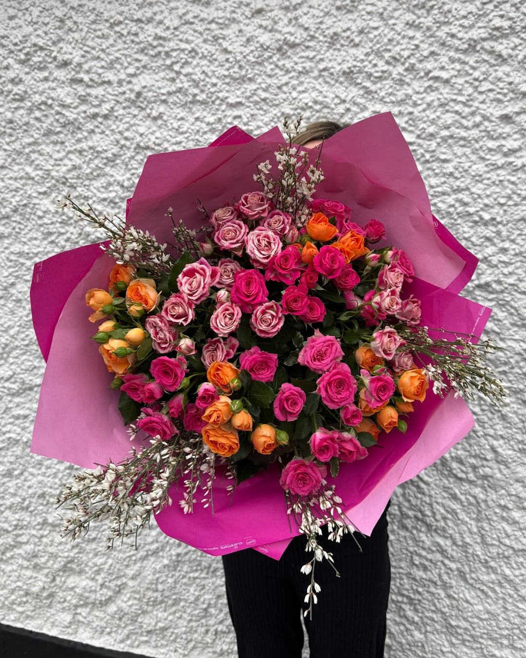 Bouquet of pink and orange flowers wrapped in pink paper against a white wall.