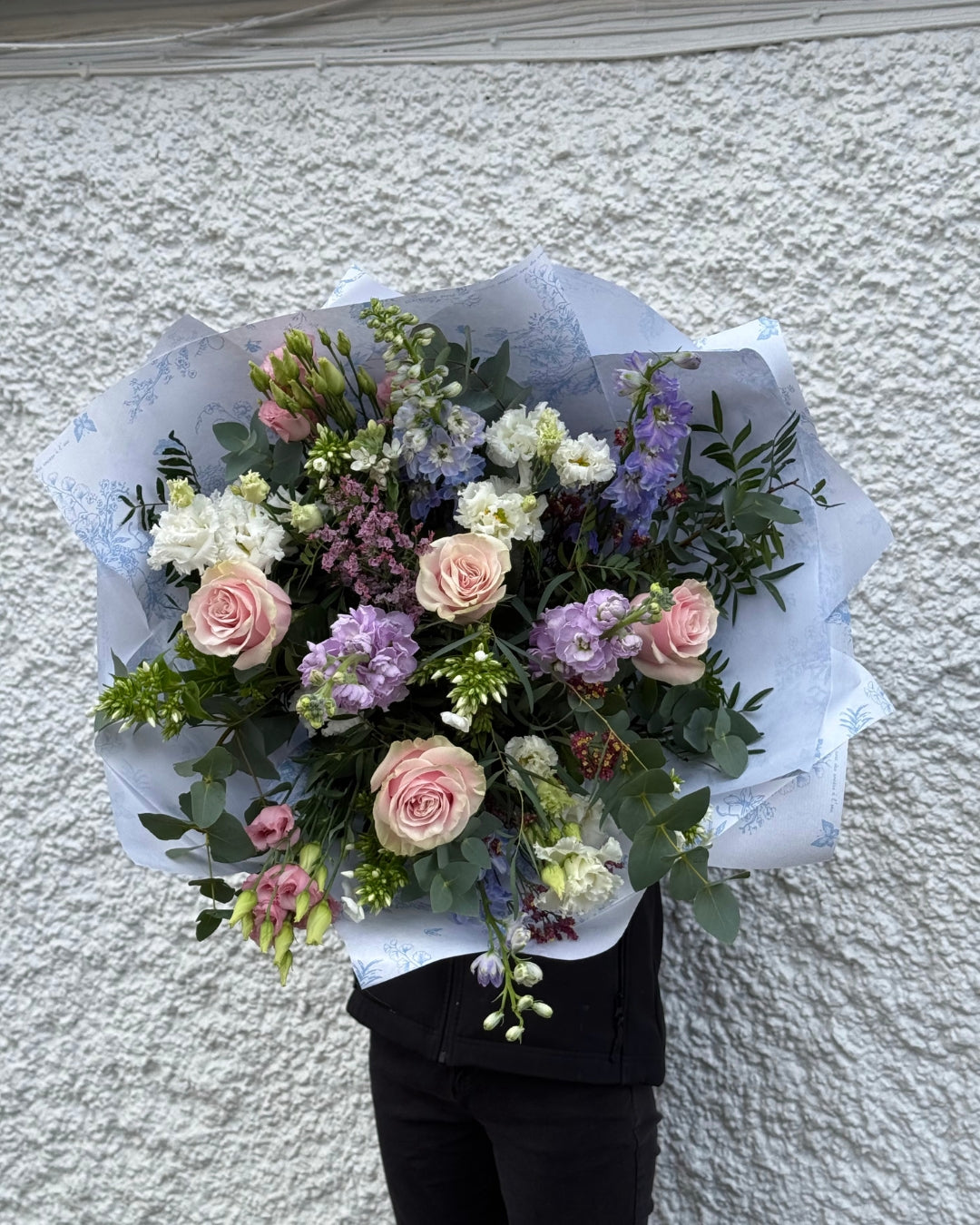 Bouquet of flowers held against a textured white wall