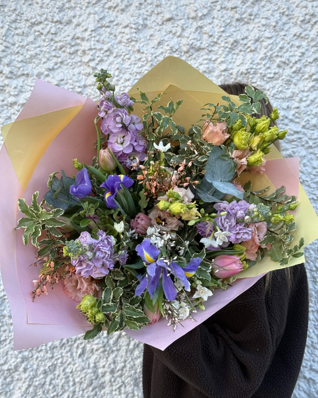 Bouquet of pink and purple flowers held by a person against a light background