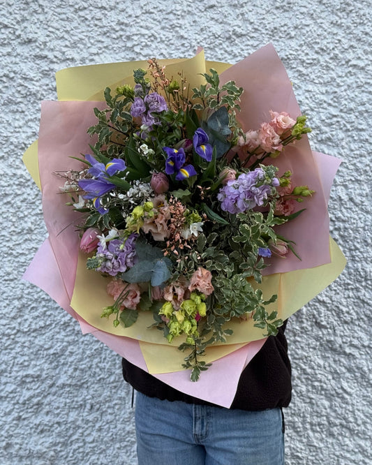 Bouquet of pink and purple flowers with mixed foliages held against a textured wall