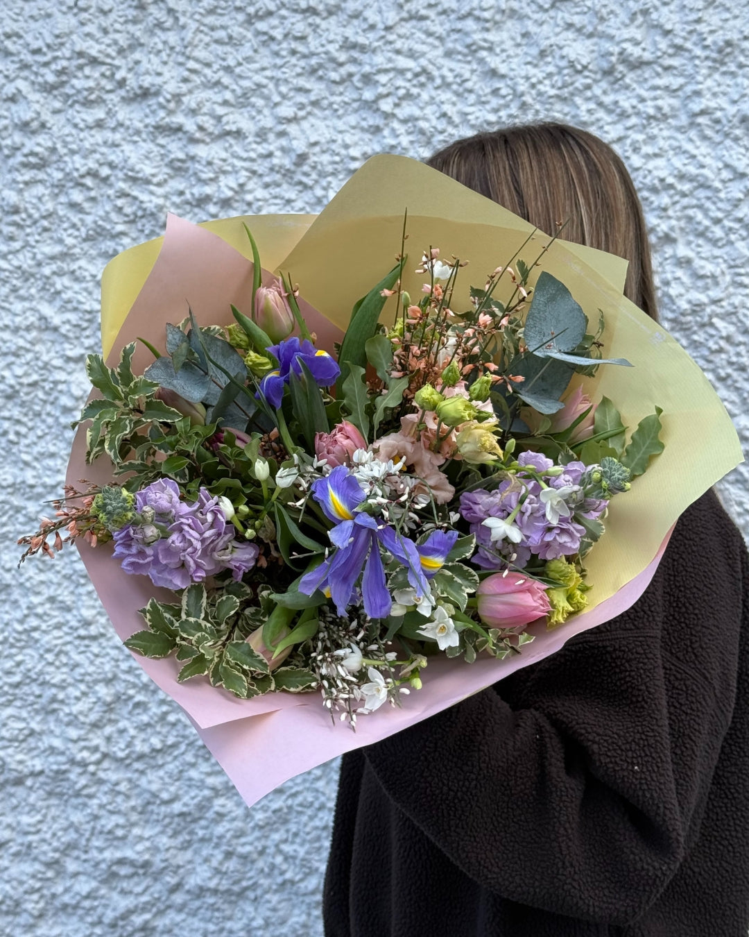 Bouquet of pink and purple flowers held by a person against a textured wall.
