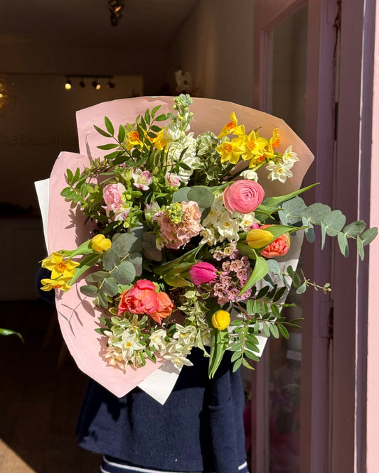 Bouquet of flowers wrapped in pink paper held by a person.